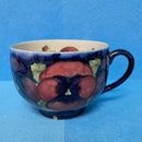 A Moorcroft Cup and Saucer in the Pansy Pattern by William Moorcroft