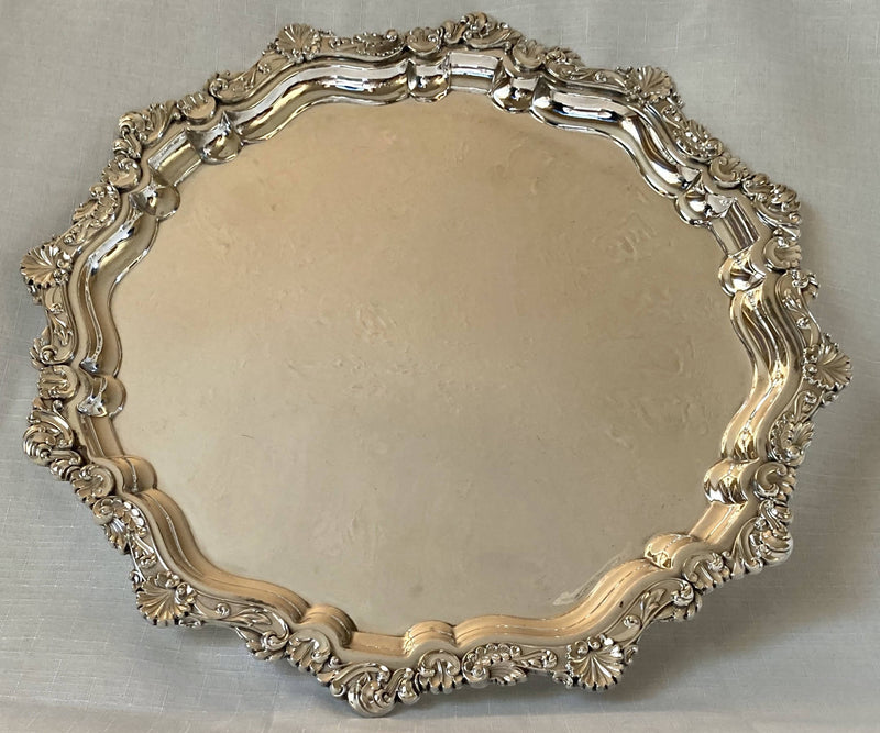 Large silver plated circular salver with shell and scroll border, raised on bun feet.